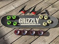 Full skateboard deck with Grizzly griptape, eight green and beige Bones STF wheels, two Thunder trucks, four Road Rider 72s wheels, and black Unit skate tool on wooden surface.