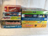 Lot of 10 classic board games stacked showing titles and branding including Yahtzee, Operation editions, Trouble, Twister, Superfection, and others.