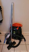 Full view of Atrix ERGO vacuum with orange power cord, metal extension wand, and attachments arranged on floor.