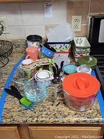 Overview of all bakeware and kitchen utensils arranged on countertop including Pyrex measuring bowls, Temptations loaf pans, small bowls, sifters and kitchen brushes.