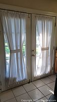 White sheer curtains on white French doors with rods and tiebacks.