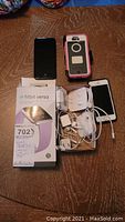 Photo showing lavender Fitbit Versa Lite in box, two iPhones, earbuds, and chargers on wooden surface.