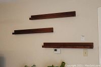 Three dark wood floating shelves mounted on a beige wall with a visible thermostat and light switch nearby, showing size and finish.