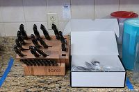 Cutco wooden knife block loaded with knives displayed beside open Lenox flatware box on countertop