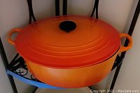 Orange enameled cast iron round Dutch oven with lid on metal rack.