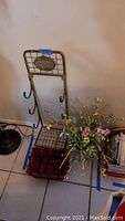 Full view of metal wire basket stand with faux floral arrangement inside and plaid basket below