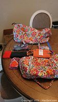 Two large floral print Vera Bradley totes, pink triangle coin purse, three smaller wallets and coin purses on round wooden table