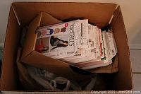 Box of mixed sewing patterns and fabrics showing McCall's patterns on top, fabrics seen inside box and plastic bags at bottom