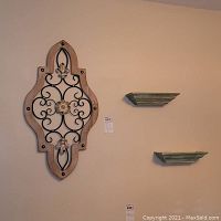 Photo showing two floating wall shelves mounted on a wall next to a Fleur de Lis wood and metal wall art piece.