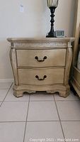 Front view of the wooden chest showing the two drawers with dark metal handles and carved decorative patterns on top and drawer fronts.