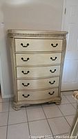 Front view of the wood five-drawer chest showing all drawers and ornate handle hardware.