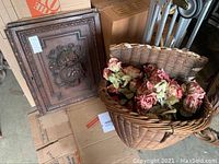 Two carved wooden doors with grape and barrel carvings, alongside a large wicker basket filled with artificial pink and red flowers.