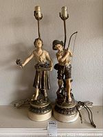 Full view of both figurine lamps side by side showing the girl with flowers and boy with fishing rod figurines and lamp sockets without shades.