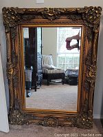 Full view of rectangular mirror with ornate gold-tone frame and beveled glass reflecting room interior