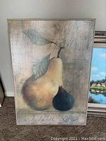 Front view of framed pear artwork showing yellow pear and smaller dark fruit with leaves against muted background.