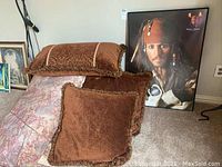 Wide shot showing all three pillows stacked and the framed poster leaning against the wall.