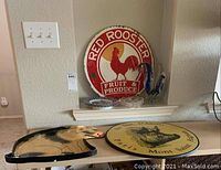 Photo showing Red Rooster Fruit & Produce metal sign on wall shelf with some plates and glass rooster figurine nearby, pig-shaped tray and round pig plate on table below.