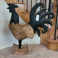 Photo showing left-side view of the wooden rooster statue with detailed tail and base visible.