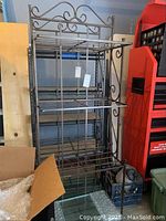 Full view of metal shelving unit with glass shelves and scrollwork design on top and sides.