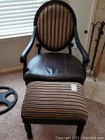Wooden side chair with upholstered oval back and black leather seat. Upholstered striped ottoman in front of chair.