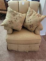 Front view of beige upholstered side chair with two matching floral decorative pillows on seat.