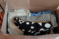 Box of handmade sweaters including a black and white geometric pattern sweater and other folded knitwear items in beige and blue.