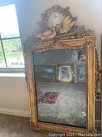 Full view of the tall rectangular gilt mirror leaning against wall, showing overall frame design, crest and glass.