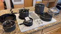 Overview of all cookware items arranged on stove including Calphalon pots and pans, vintage cast iron skillets, and aluminum roaster lid