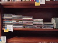 Photo showing around 50+ CDs stacked on wooden shelf with small CD rack empty on bottom shelf