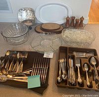 Overview photo showing the silver plate flatware on brown trays, clear glass bowls, divided dishes, wooden cutting boards, and pepper mills.