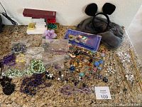 Wide view of lot showing necklaces, earrings, neck rice pillow, and pliers kit on countertop.