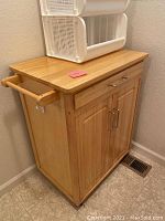 Front angle view of wooden kitchen island cart showing flat top, drawer, dual cabinet doors, and towel rack on the side.