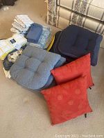 Overall view of kitchen linens piled and a variety of seat cushions including red, blue, and gray with memory foam padding.