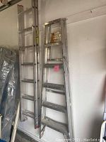 Photo showing side view of a 6ft step ladder with paint marks and an extension ladder hanging on the wall, both made of aluminum.