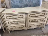Front view of the large cream-colored dresser showing gold decorative trim and floral carvings on drawers