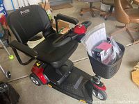 Oblique view of Pride Go-Go Elite electric mobility scooter showing black vinyl seat with flip-up armrests, red chassis, foot platform, and front wire basket attached to tiller