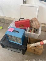 Wide photo of various tools and hardware containers including blue metal organizer, black and red toolboxes, plastic bin, and cardboard box.