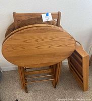 Set of four wooden tray tables with oval tops, arranged standing, shown from side showing folded legs and from front.