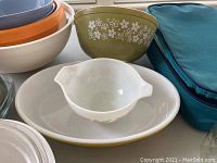 Full view of various mixing bowls including vintage Pyrex floral pattern bowl, milk glass promotional bowl, and contemporary colored bowls stacked