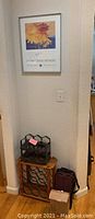 Framed signed wine print from Plum Creek Winery hung on the wall above two wine racks and a box