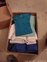 Two boxes of folded women's tops and blouses in size XL, various colors including teal, light green, white with stripes, and blue.