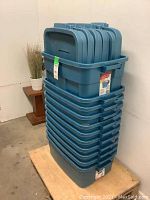 Stacked 11 blue Rubbermaid storage bins with lids, showing 10 short bins and 1 deep bin in blue plastic, stacked on a wooden pallet.