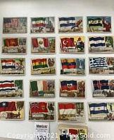 Photo showing a set of 21 vintage Flags of the World trading cards laid out in rows, featuring flags of multiple countries including United States, Iran, Ceylon, Peru, Union of South Africa, Bolivia and others. Cards show wear and creasing.