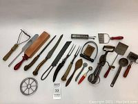 Full view of all 20 antique kitchen utensils arranged in white background showing various types and handle styles, including some with antler handles