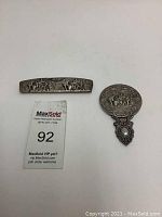 Pocket mirror and comb laid flat on white surface showing hand tooled silver plating and village scenes