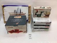 Overview of all four items in the lot including a wooden dish rack, boxed silicone bakeware set, wrapped spice rack and apple machine in original box.