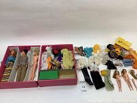 Opened pink vinyl Barbie doll trunk showing multiple compartments with vintage dolls and various clothing and accessories, doll clothes are mixed and include handmade and store-bought pieces.