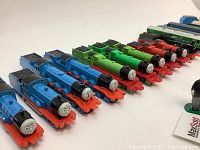 Close-up view of the die-cast Thomas the Train engines showing blue, green, and red train models with detailed faces and coal loads on top.