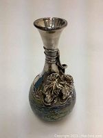 Full front view of the vase against a plain background showing the flared silver neck and leaf motif.