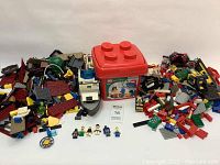 Wide view of the collection showing many loose Lego pieces, minifigures, partially built sets including a police boat, and a large red Lego brick-shaped storage container.